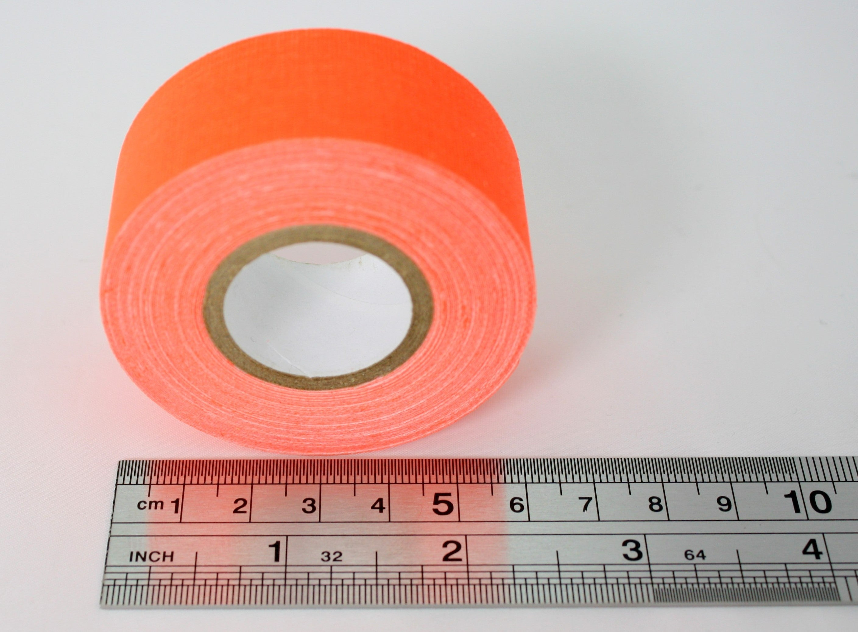 A close up of a single roll of fluorescent orange Micro Gaffer 1" tape. The roll is next to a metal ruler showing that the widest part is just over 6cm